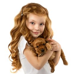 Young girl with curly hair smiling and holding a small brown puppy.