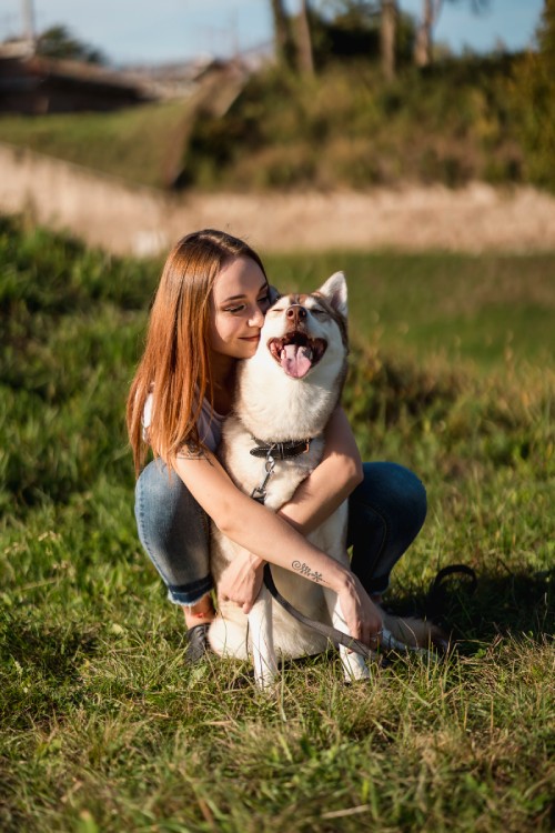 Woman hugging a happy Siberian Husky in a grassy field.