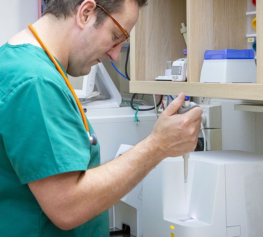 A male nurse in green scrubs using medical equipment in a clinic.